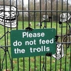 This meme is an image of a "do not feed the trolls" sign, a common warning found at parks and other public areas, but it has been altered to include the face of a troll character from the internet. The sign now reads "do not feed the trolls" but the text is replaced with "do not feed the trolls" in a font that looks like it's been written in a messy, handwritten style, similar to a troll's online persona.